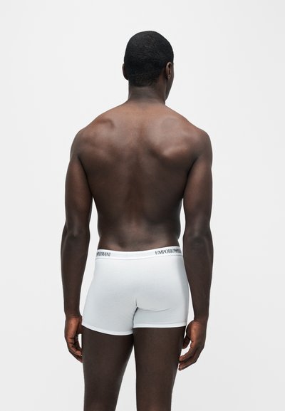 Άνδρας από πίσω, φορώντας λευκά boxer της Emporio Armani σε απλό ανοιχτό φόντο.