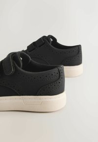 Melnas kedas ar gludu, matētu virsmu, perforētām detaļām, Velcro aizdari un vieglu gumijas zolīti.