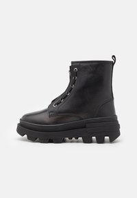 Botas de cuero negras hasta el tobillo con una suela gruesa, que presentan ojales de metal, diseño de cordones y puntera redonda. Suela estriada para mayor tracción.