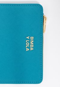 Cartera de tela en color azul verdoso con cierre de cremallera, que presenta el logo dorado "BIMBA Y LOLA" grabado en la parte frontal. Textura suave y forma rectangular.