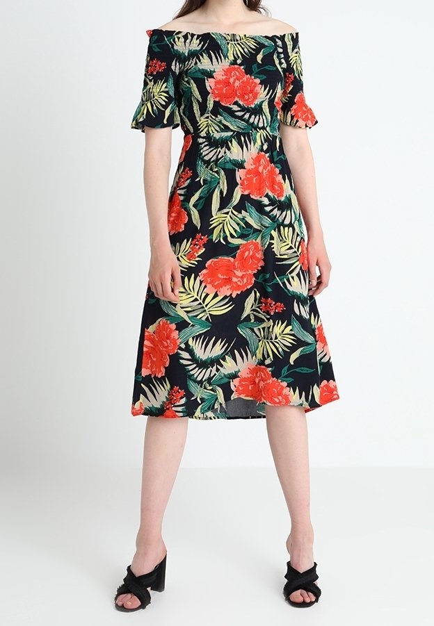 Robe florale décolletée avec des fleurs rouges et jaunes sur un fond noir, dotée de manches courtes et d'un corsage ajusté, se prolongeant jusqu'aux genoux.