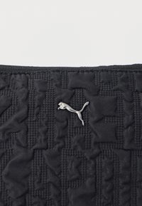 Μαύρο καπιτονέ ύφασμα με ένα μικρό ασημένιο λογότυπο πάνθηρα στο κέντρο, που δείχνει την υφή και τις λεπτομέρειες ραφής.