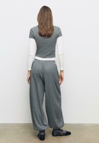 Sivi rebrasti hlače s labavim krojem i elastičnom strukom; uparene s majicom kratkih rukava sive boje koja je složena preko bijele majice s dugim rukavima.