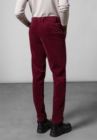 Burgundské manšestrové kalhoty s přizpůsobeným střihem, s kapsami na zadní straně a hladkou texturou, v kombinaci s černou obuví.