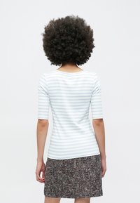 Lys blå og hvit stripete tilpasset topp med korte ermer, kombinert med et teksturert mørkt skjørt, sett bakfra.