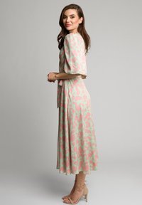 Kwiatowa sukienka midi z miętowo-zielonym tłem i różowym nadrukiem kwiatów, krótki puffowe rękawy oraz z wcięciem w talii. Połączona z cielistymi sandałami na paski.