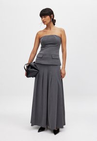 Grau, trägerloses Kleid mit einem Peplum-Taille, gefaltetem Rock und zwei vorderen Taschen. Kombiniert mit einer schwarzen geometrischen Handtasche und spitzen Absätzen.