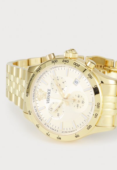 Zlaté hodinky Versace so zaobleným ciferníkom, prepojeným náramkom, chronografickými ciferníkmi, zobrazením dátumu a textúrovaným rámčekom s logom značky.