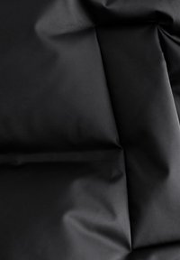 Black fabric displaying a smooth, matte texture with soft folds and subtle variations in sheen, emphasizing its pliability and depth.