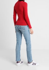 Červený top s dlouhým rukávem a žebrovanou texturou, spárovaný s světle modrými slim-fit džíny a bílými teniskami s fialovými akcenty. Celkově jednoduchý design.