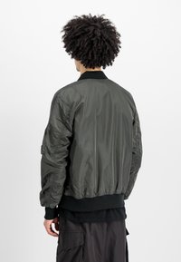 Groene nylon bomberjack met een geribde kraag, elastische manchetten en een zoom. De achterkant heeft een doorgestikte textuur en minimale details.