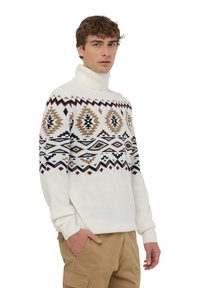 Biała, dziana na drutach bluzka z golfem z geometrycznymi wzorami w kolorze brązowym, czarnym i burgundowym. Rękawy i dół ze ściągaczem, luźny krój.