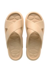 Beige cross-strap sandals made of rubber. Textured footbed with oval patterns and a smooth finish. Brand name visible on the side.