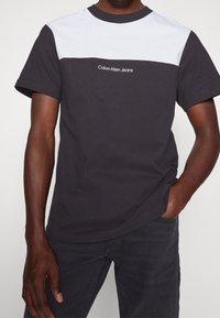 Camiseta de color bloque en blanco y negro con el logo bordado "Calvin Klein Jeans" en el pecho. Fabricada en algodón con un diseño de cuello redondo.