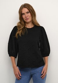 Top negro texturizado con mangas abullonadas, cuello redondo y puños elásticos. Combinado con jeans azules que presentan un sutil patrón geométrico.