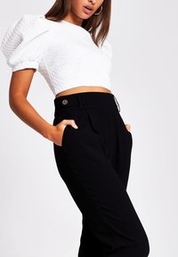 White textured crop top with puff sleeves paired with high-waisted black trousers featuring side pockets and gold button detail.