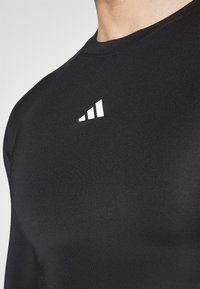 Zwarte sportshirt met ronde hals, strakke pasvorm en een gladde textuur. Bevat een wit logo op de bovenste linkerborst.