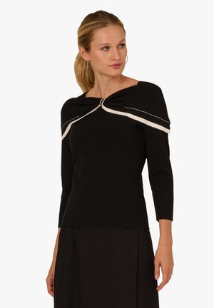 Schwarzer Pullover mit dreiviertel Ärmeln, versehen mit einer gedrehten Knotendetail am Ausschnitt und weißen Ziernähten entlang der Kanten.