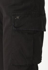 Černé cargo kalhoty s bočními kapsami a stříbrným logem "M". Vyrobené z odolné tkaniny s hladkým povrchem a zesílenými švy.