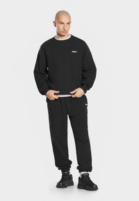 Czarna bluza z ribbowymi mankietami, luźny krój i biały logo. W połączeniu z czarnymi dresami z bocznym logo oraz czarnymi sneakerami.