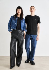 Chaqueta de mezclilla de color azul claro, camiseta negra, pantalones de cuero sintético negros, jeans azules y zapatos negros de suela gruesa, diseño minimalista.