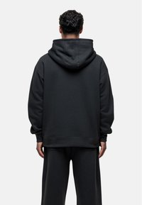 Felpa nera con cappuccio realizzata in tessuto morbido, caratterizzata da una vestibilità ampia, polsini a coste e una tasca a marsupio, vista da dietro.