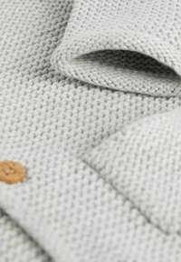 Gray knitted fabric with a textured pattern. Features a wooden button and folded edge, showcasing soft, warm fabric quality.