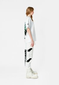 Camiseta blanca con diseño de mariposa, combinada con pantalones blancos que presentan patrones de alas negras y una franja gráfica negra en el lateral. Usado con botas blancas.