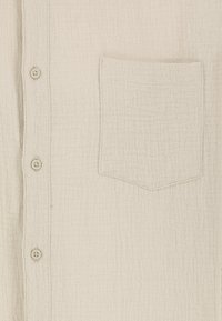 Helles beiges Button-Up-Hemd aus strukturiertem Stoff. Verfügt über eine einzelne Brusttasche und fünf Knöpfe auf der Vorderseite, mit dezenten Stichdetails.