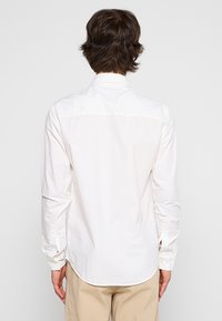Witte langek mouwen shirt met een gebogen zoom, knoopmanchetten en een subtiele textuur. De achterkant toont een licht gestructureerd ontwerp.