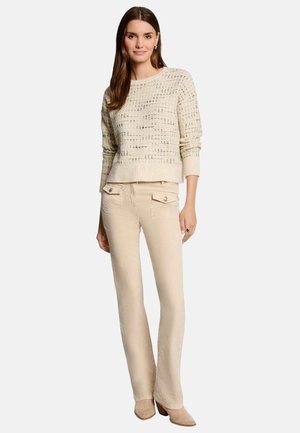 Pull en tricot beige avec un motif texturé, associé à un pantalon droit beige clair avec des poches avant et de subtils détails de boutons.
