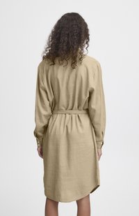 Rochie cămașă bej, cu mâneci lungi, talie brăzdată, croi lejer și tiv curbat. Confecționată dintr-un material texturat asemănător cu in.