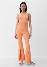 Geribbeld, mouwloos oranje topstuk gecombineerd met uitlopende, hooggespleten oranje broek. Glad materiaal met een aansluitend ontwerp en een brede tailleband.