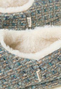Woven slippers with a blue, brown, and metallic-thread pattern. Soft, cream-colored faux fur lining and tag visible on the side.