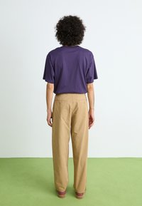 Purple, short-sleeved t-shirt paired with beige, loose-fitting trousers and brown platform shoes. Minimalist design against a light background.