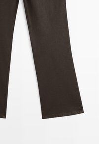 Donkerbruin rechte broek met zichtbare naden, weergegeven op een witte achtergrond, die de onderste helft van de benen toont.