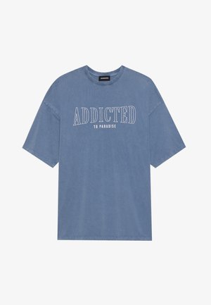 Blaues, übergroßes T-Shirt aus weichem Stoff mit Rundhalsausschnitt. Der Frontdruck lautet "ADDICTED TO PARADISE" in weißen, fetten Buchstaben.