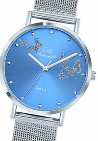 Montre en quartz ronde en argent avec un cadran bleu, accentué par des motifs de papillons et des strass. Elle est dotée d'un bracelet en métal tissé.