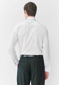 Biała koszula z długim rękawem, o usztywnionym kołnierzu, z mankietami zapinanymi na guziki oraz gładkiego materiału, zestawiona z czarnymi spodniami garniturowymi i czarnym paskiem.