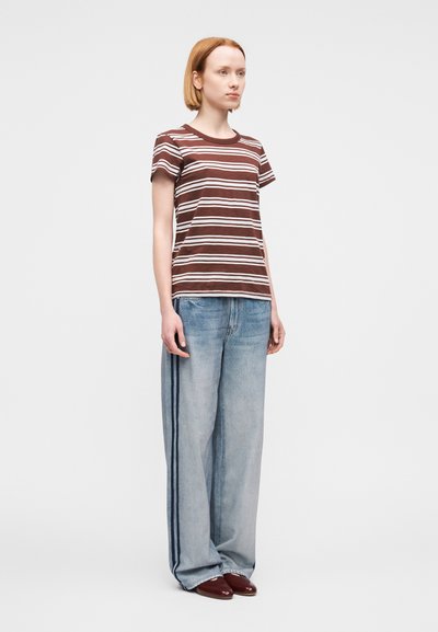 Καφέ και λευκή ριγέ μπλούζα με κοντά μανίκια, σε συνδυασμό με φαρδιά ανοιχτό μπλε τζιν παντελόνια με ρίγες στο πλάι, φορεμένα με καφέ παπούτσια.