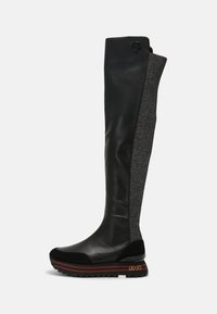Stivale in pelle nera altezza ginocchio con un pannello in tessuto grigio texture. Presenta una suola spessa con piattaforma e dettagli decorativi in rosso.