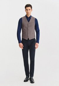 Szara kamizelka na granatowej koszuli, z sześcioma guzikami i kieszenią na piersi. Połączona z ciemnymi spodniami i czarnymi eleganckimi butami, tworzy formalny wygląd.