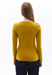 Top giallo a maniche lunghe con scollatura rotonda, design aderente e texture liscia, abbinato a jeans blu scuro con cuciture a contrasto.