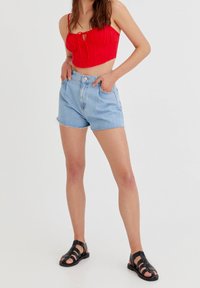 Red cropped top with tie detail, blue denim shorts with frayed hem, and black strappy sandals. Cotton material, casual design.