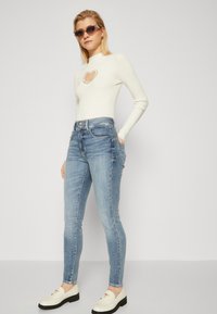 Hvid ribbet langærmet top med hjerteudskæring, parret med lyseblå skinny jeans med sidelommer med lynlås og off-white slip-on sko.