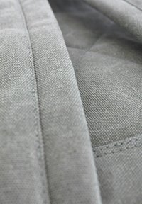 Grau gestepptes Gewebe mit einer strukturierten Webart und sichtbaren Nähten, das eine glatte, strapazierfähige Oberfläche und geometrische Musterdetails zeigt.