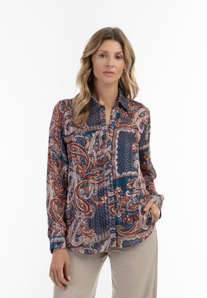 Camicia a maniche lunghe in tessuto setoso con motivo paisley e geometrico in blu, ruggine e crema. Chiusura frontale con bottoni e taschino a toppa.