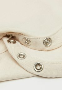 Tkanina krémové barvy s ribbovanou strukturou, s kovovými stříbrnými druky podél okraje. Hladký povrch s jemným leskem.