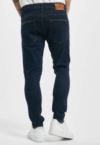 Tummansiniset farkut, joissa on slim fit -malli, takataskut ja kontrastiväriset tikkaukset. Yhdistä valkoisten tennareiden kanssa.
