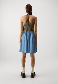 Halter stílusú top, ráncolt olíva szövetből, világoskék farmer szoknyával párosítva, deréknál megkötve. Barna, vastag talpú cipők.